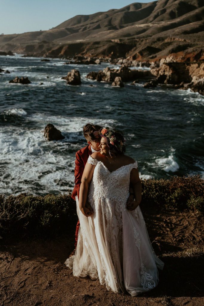 Couple Cuddled together during their elopement on the cliffs over looking the Ocean in Big Sur California 