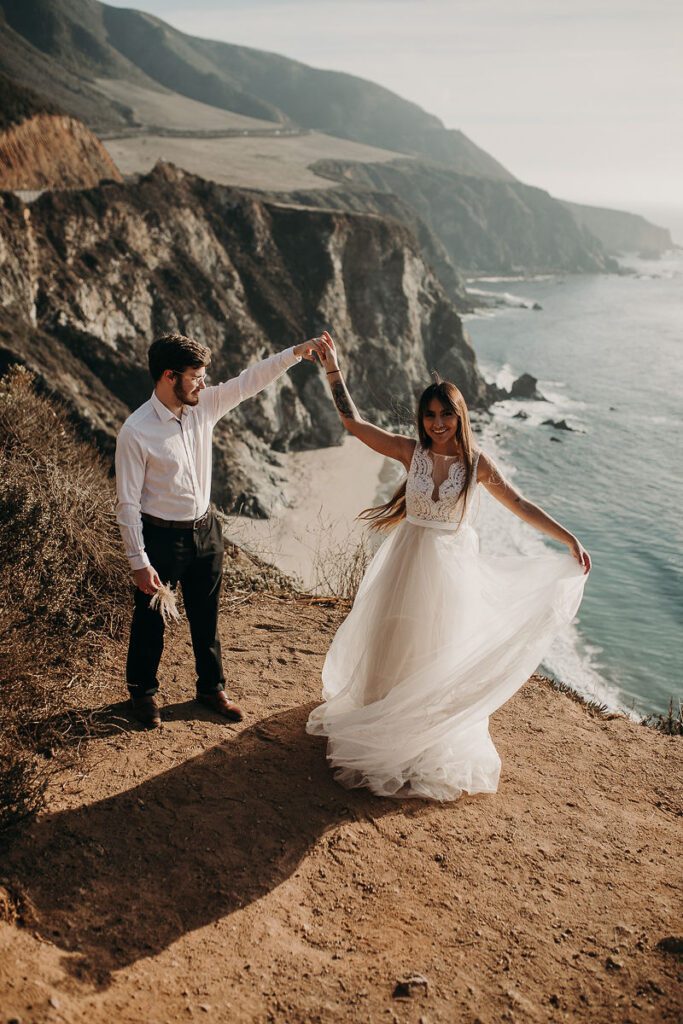 Eloping Couple on a cliff, groom is spinning his bride while over looking the ocean