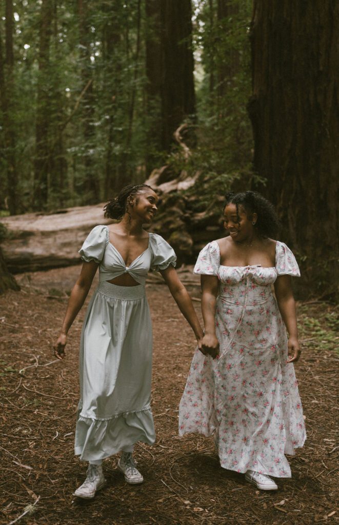 Couple walking towards the camera looking at each other surrounded by the redwoods.