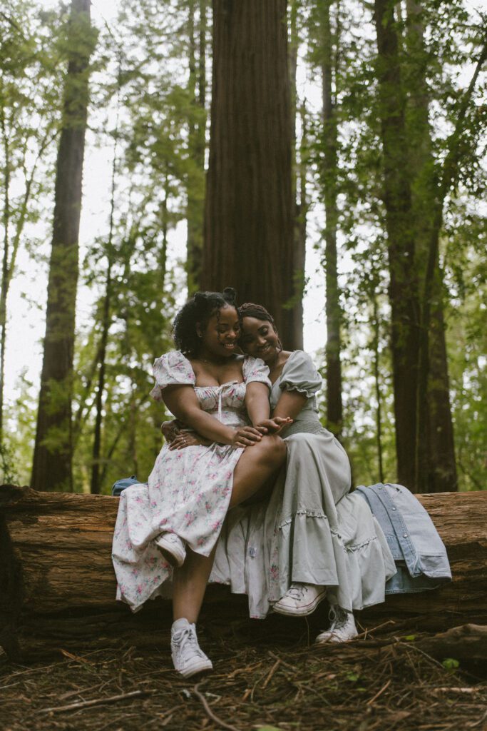 Engagement photos of Lesbian couple cuddled on a fallen redwood tree in the Redwood National Forest 